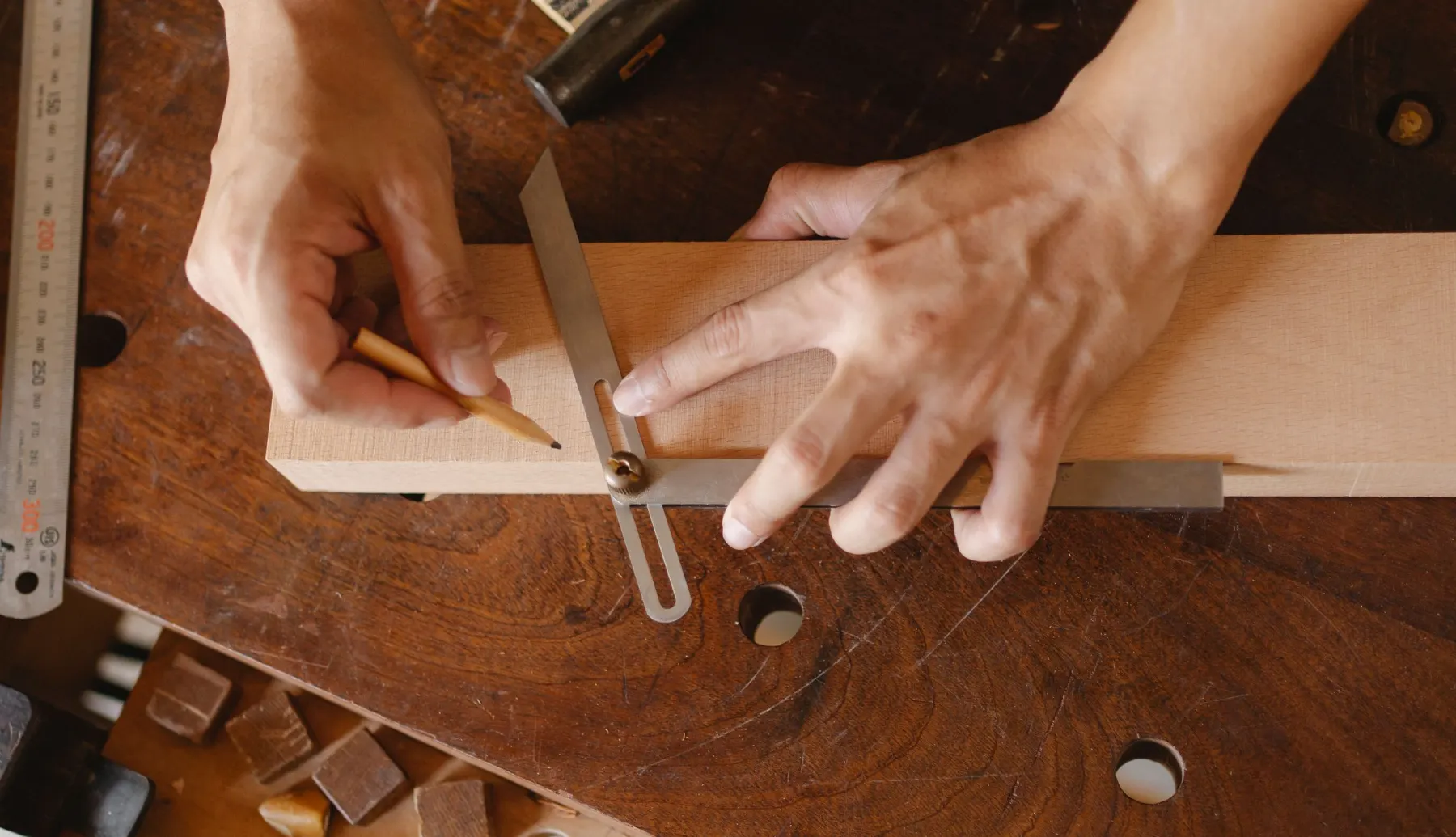 Hände zeichnen mit Bleistift und Winkel eine Linie auf ein Holzbrett, von oben gesehen