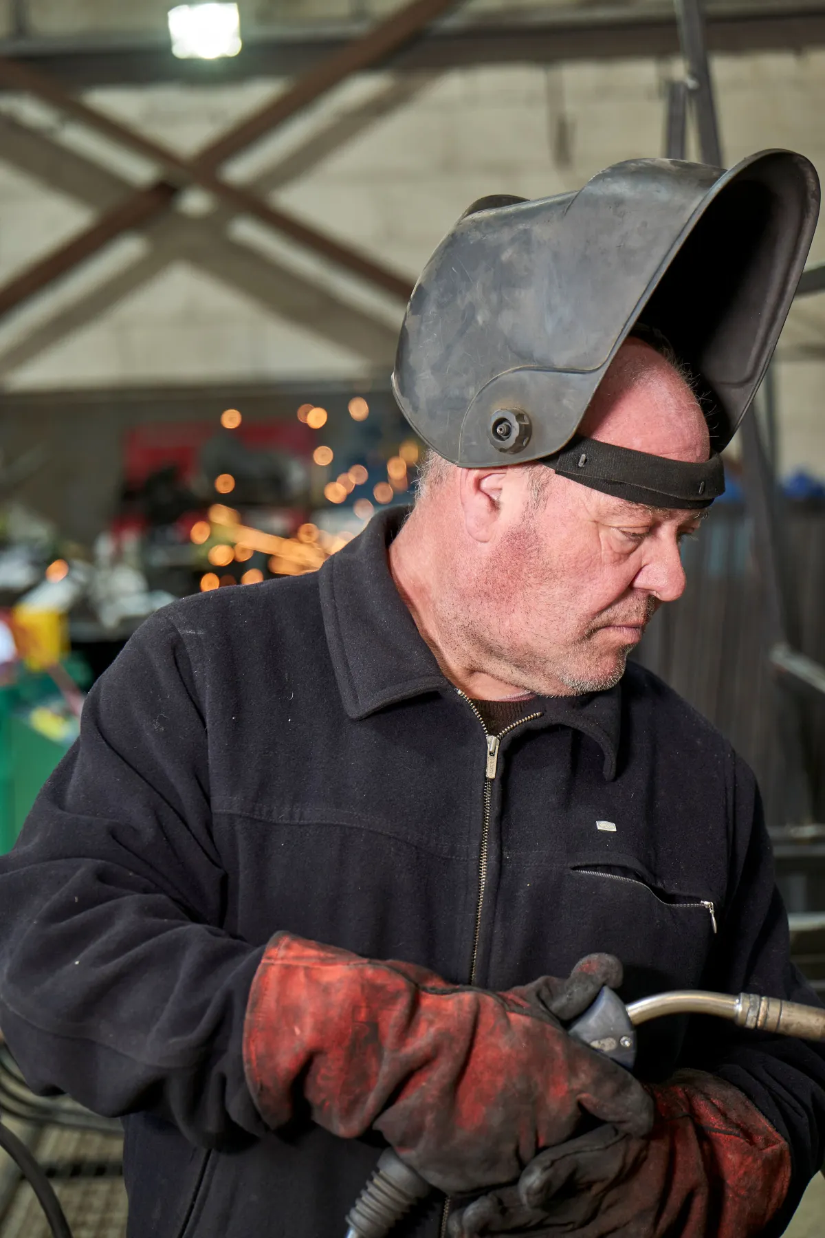 Ein Schweißer mit hochgeklapptem Schutzhelm hält einen Brenner in der Werkstatt